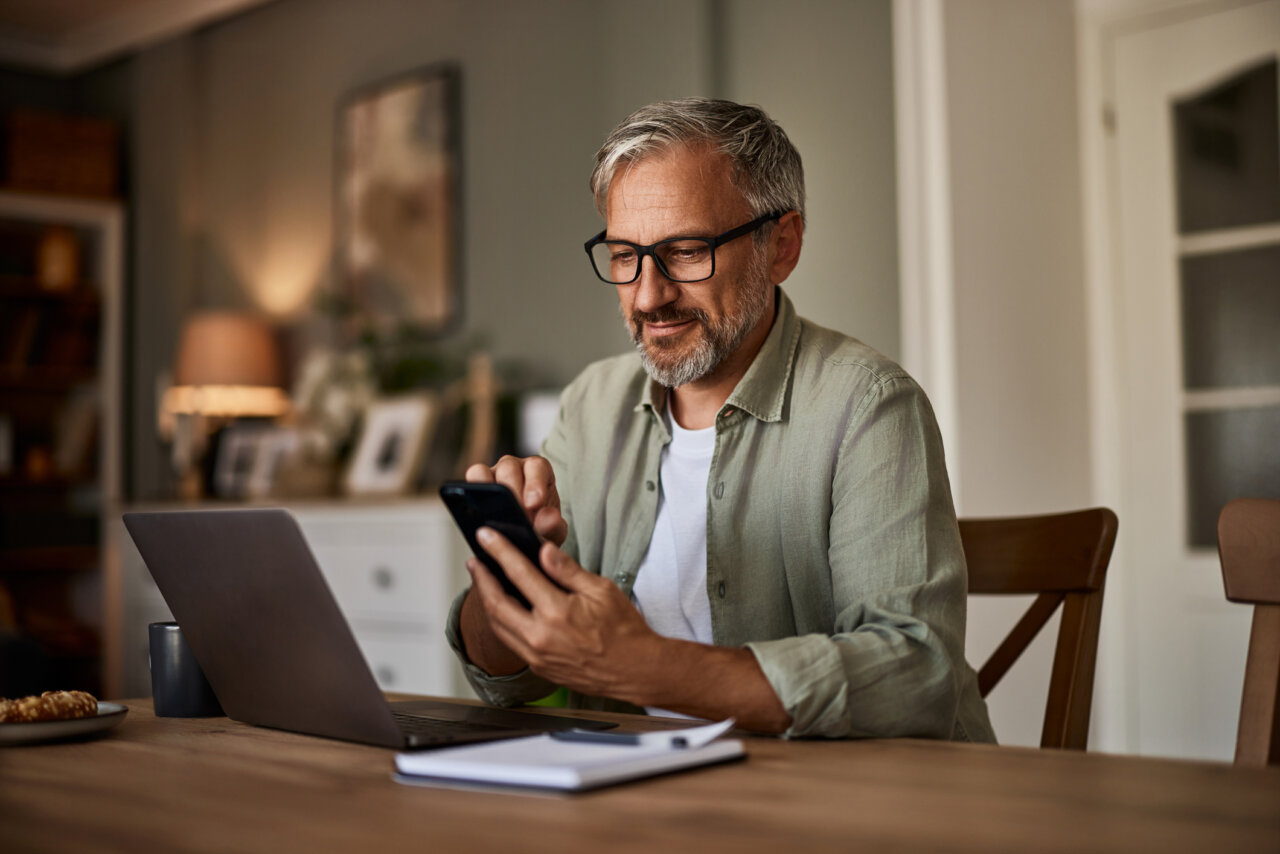 en företagare kollar på mobilen och datorn och undrar om han behöver ha tjänstepension.
