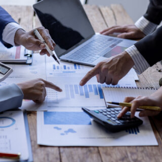 Flera händer som pekar på papper med grafer och siffror.